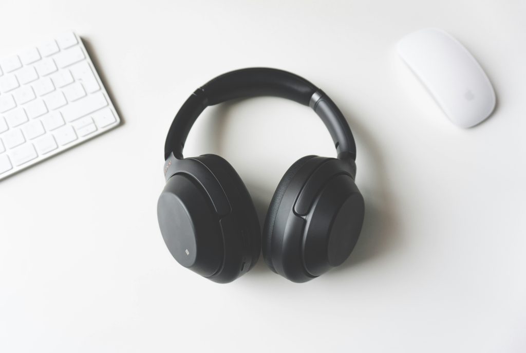 Black over-ear wireless headphones resting on a white desk next to a white keyboard and mouse, suitable for the best headphones 2025 guide.
